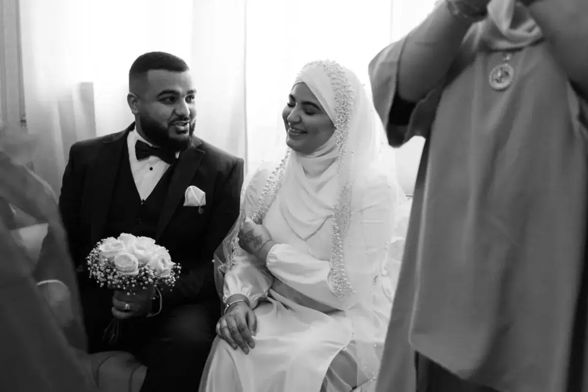 Un couple rayonnant lors de leur mariage religieux islam. Le marié, en costume, tient un bouquet. La mariée, voilée, sourit tendrement.