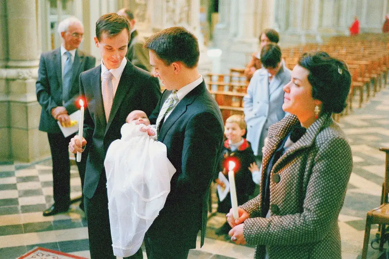 Un bébé en habit de baptême est tenu par deux hommes, l'un tenant une bougie. Combien de parrain et marraine seront présents pour ce moment solennel ?