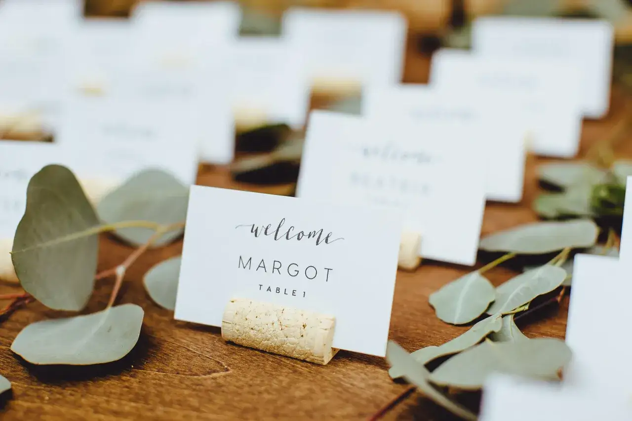 Marque place bouchon pour Margot, table 1, entour&eacute; de feuilles d'eucalyptus sur un fond en bois.
