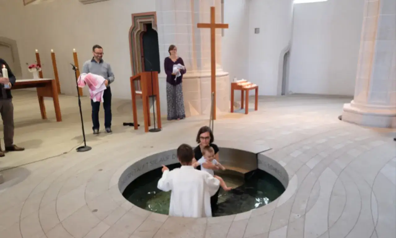 Cérémonie de baptême protestant dans une église. Un bébé est tenu par sa mère, prêt à être immergé dans la cuve baptismale.