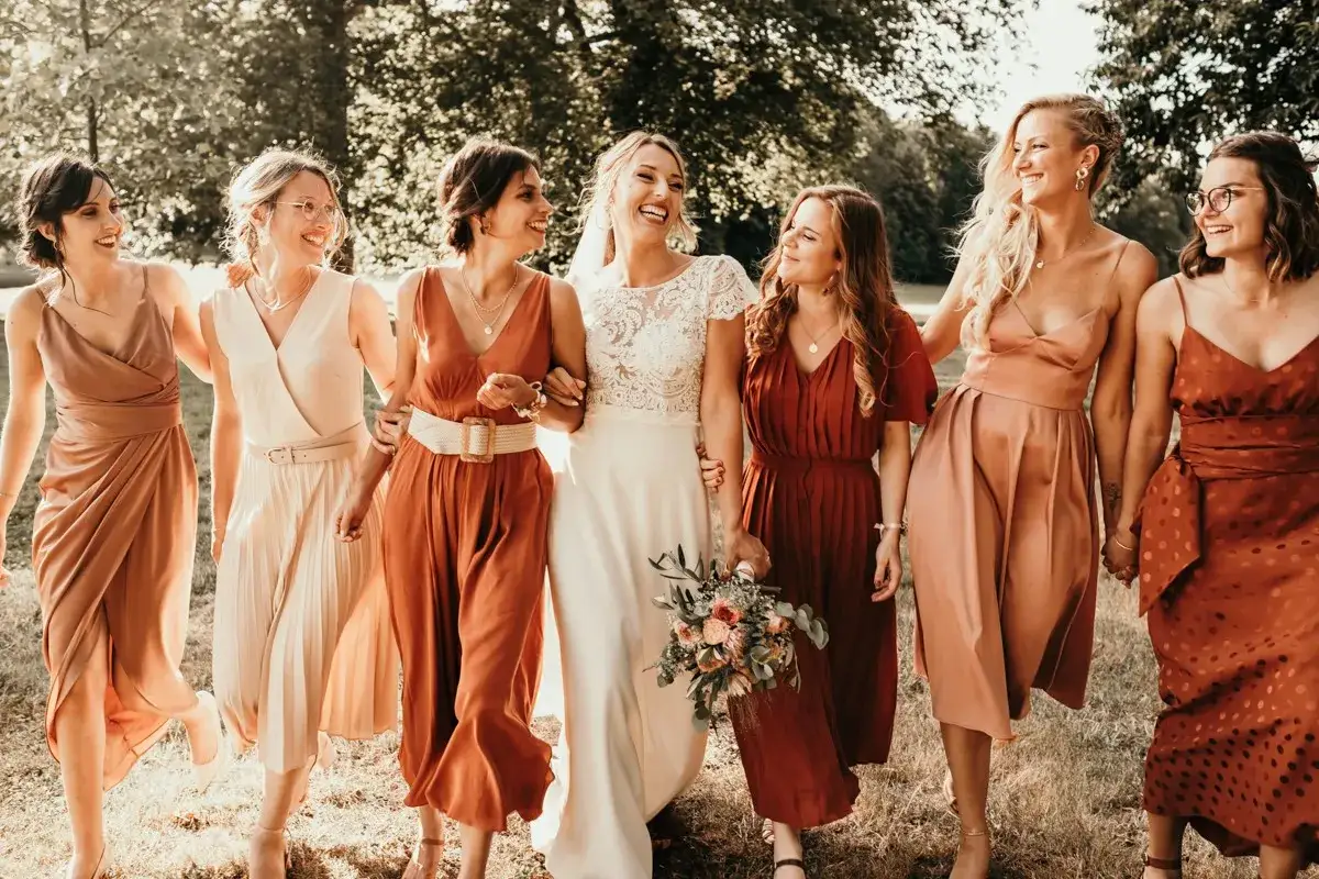 La mari&eacute;e et ses demoiselles d'honneur marchent ensemble, rayonnantes de joie. Leurs robes aux tons chauds cr&eacute;ent une harmonie parfaite pour ce mariage.