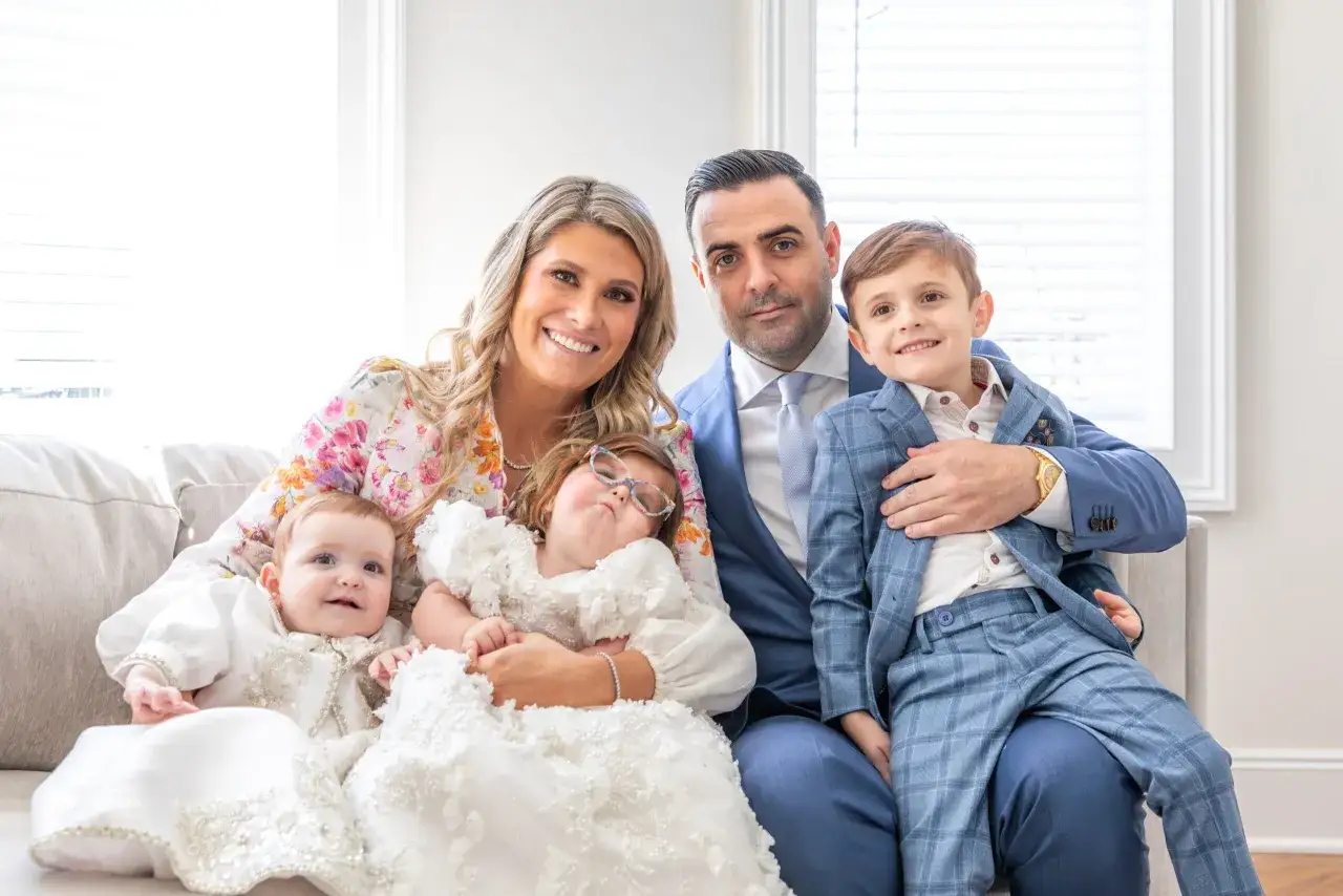 Famille réunie pour un double événement : mariage et baptême le même jour. Les parents souriants, leurs deux filles en tenues de cérémonie et leur fils en costume.