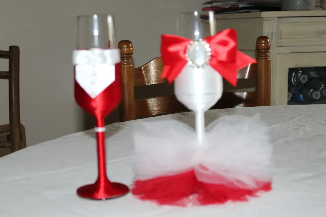 Deux flûtes personnalisées mariage, l'une habillée en smoking blanc et rouge, l'autre en robe de mariée blanche et rouge, prêtes pour la célébration.