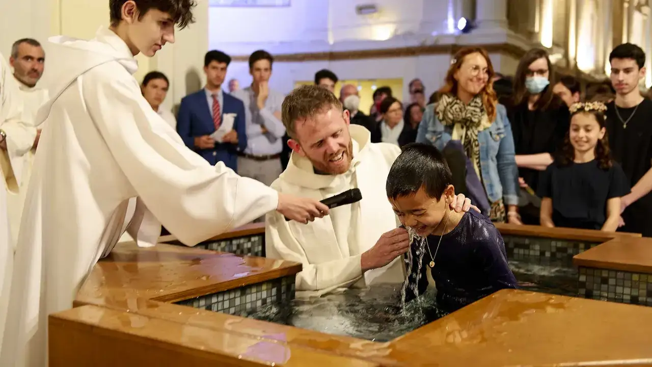 Un enfant est baptisé dans une église, l'eau ruisselle sur son visage. La durée du baptême à l'église est un moment solennel et joyeux.