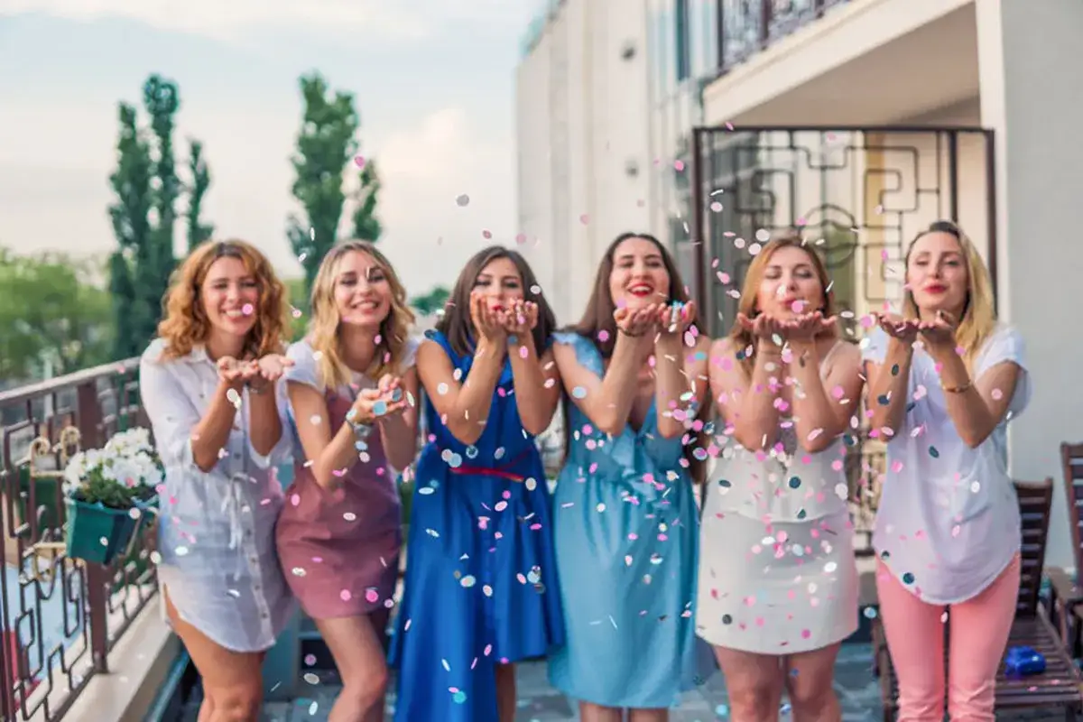 Six femmes célèbrent joyeusement, lançant des confettis. C'est une belle image qui illustre ce qu'est un evjf : un moment de partage et de fête avant le grand jour.