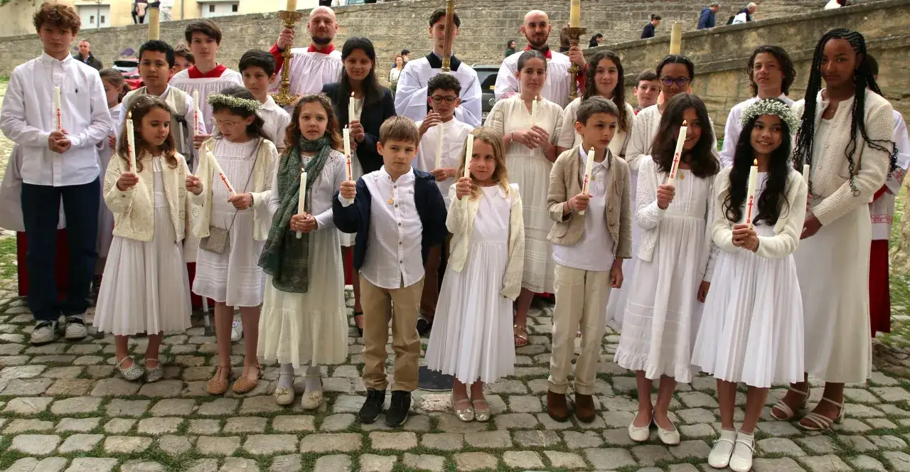 Des enfants en habits blancs tiennent des cierges allumés, une scène qui évoque la question : pourquoi baptiser son enfant ?