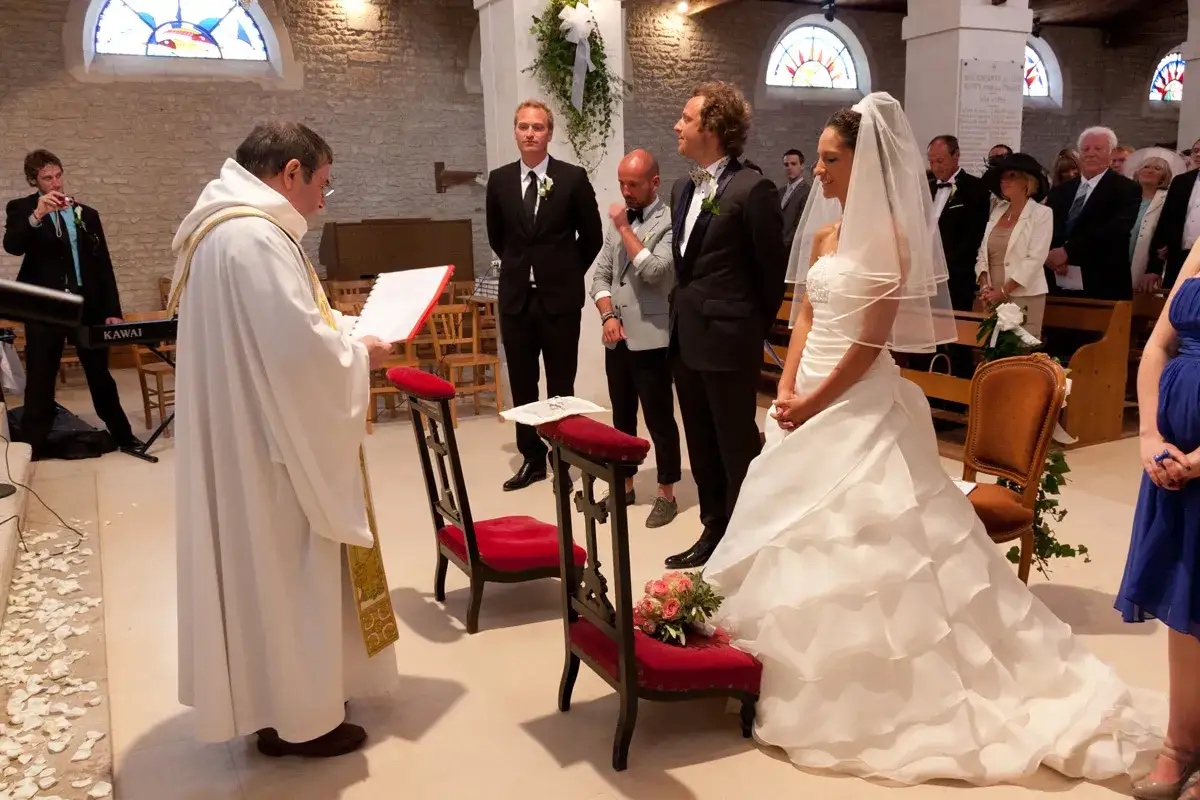 Cérémonie de mariage : le prêtre lit la prière des époux devant la mariée en robe blanche et le marié.