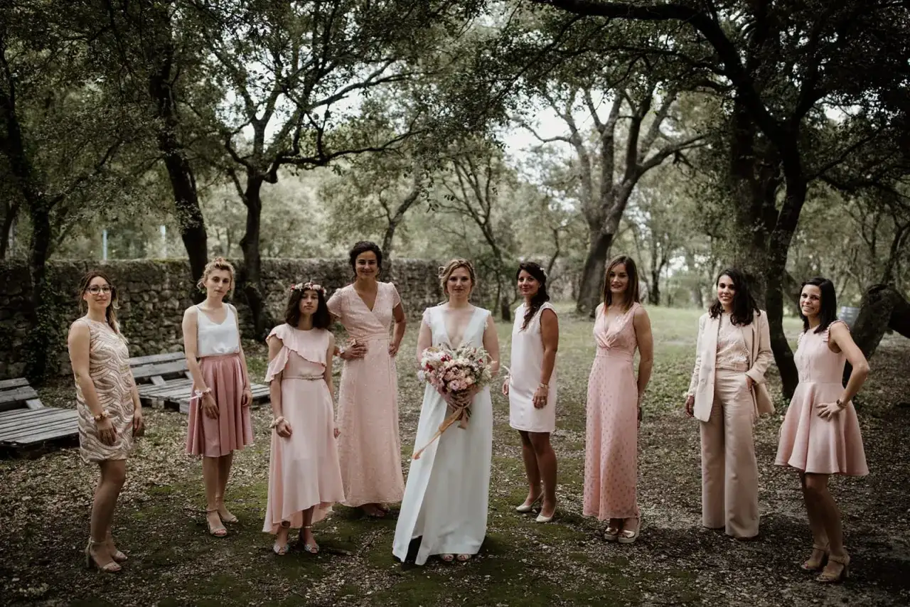 Mariée et ses demoiselles d'honneur dans des tenues roses, respectant le dress code rose, posent sous les arbres.