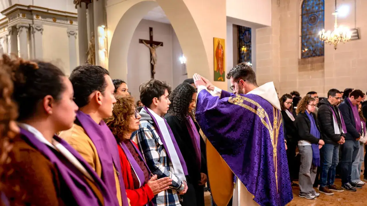 Un prêtre en chasuble violette bénit des fidèles, dont des jeunes, lors d'une cérémonie de baptême.