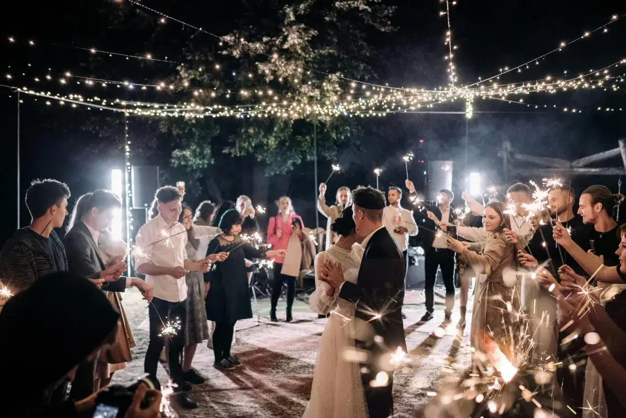 Un couple danse sous des guirlandes lumineuses, entouré d'invités tenant des feux de Bengale. L'ambiance parfaite pour une playlist mariage pour danser.