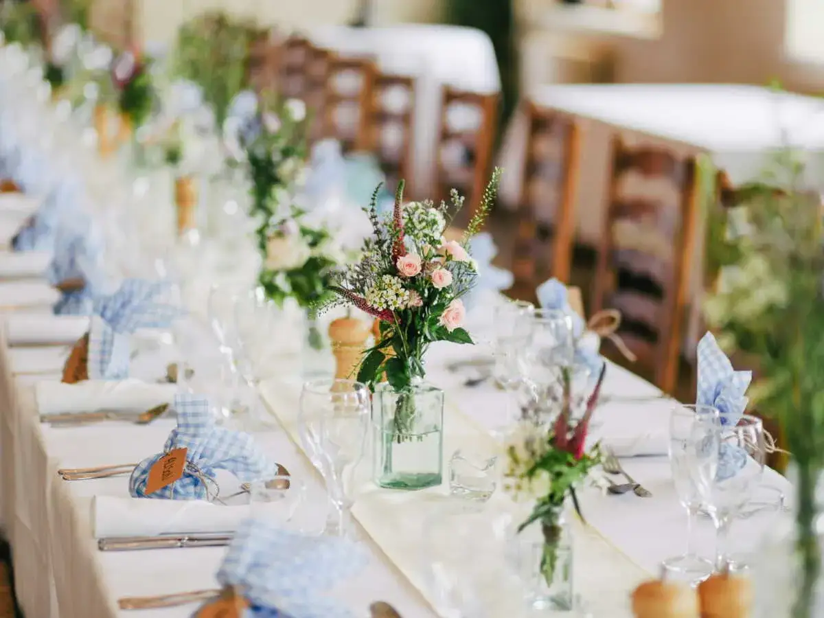 Table dressée pour un thème baptême fille original : bouquets de fleurs champêtres, serviettes à carreaux bleus et blancs, ambiance douce.