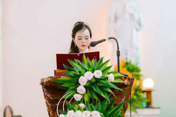 Une femme lit un texte devant un pupitre fleuri. La question "faut il etre baptisé pour etre temoin a l'eglise" résonne.