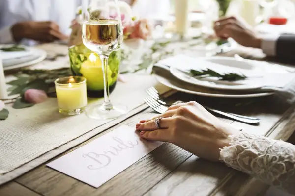 Un verre de champagne et une bougie illuminent une table dressée pour un mariage. La carte "Bride" annonce le cocktail de bienvenue.