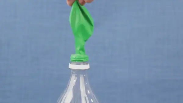 Un ballon vert est posé sur le goulot d'une bouteille en plastique. Une main le tient, prêt à montrer comment gonfler un ballon.