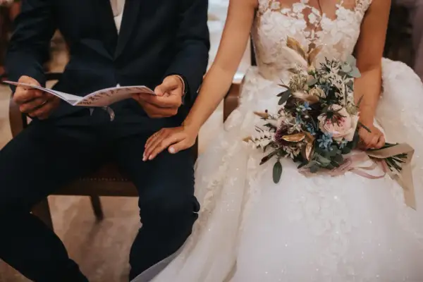 Un couple se tient la main, le marié lit un document, la mariée tient un bouquet. La musique de la sortie de mairie résonne.