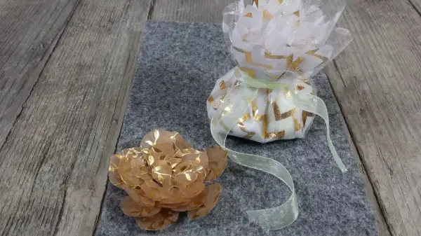 Un sachet dragees a faire soi meme, décoré de motifs dorés, à côté d'une fleur en papier.