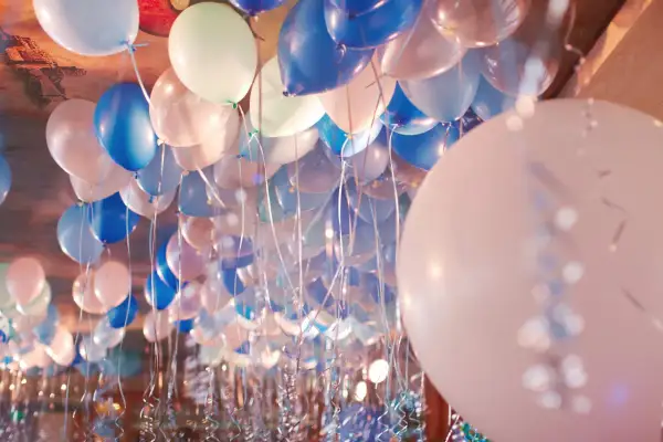 Une multitude de ballons bleus, blancs et roses flottent au plafond, prêts à gonfler avec de l'hélium pour une fête.