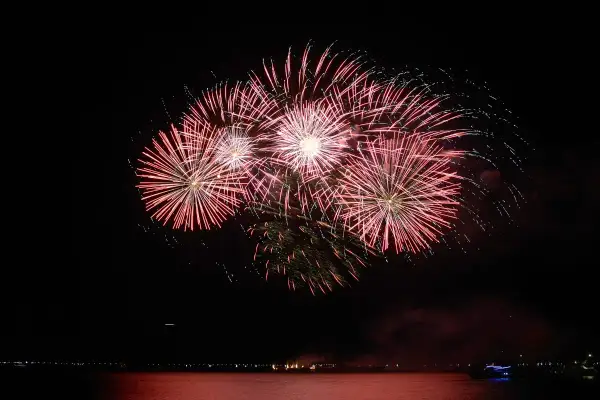 Un spectaculaire feu d'artifice illumine le ciel nocturne au-dessus de l'eau, reflétant ses couleurs vives sur la surface calme.