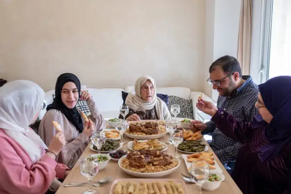 Un repas de famille pour l'Aïd el-Kebir : une grand-mère, des parents et des enfants partagent un festin copieux.