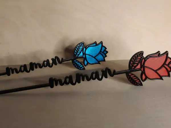Deux roses décoratives avec le prénom "maman" gravé, l'une bleue, l'autre rouge.