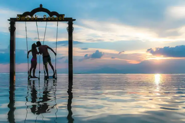 Couple s'embrassant sur des balançoires au coucher du soleil, une parfaite destination lune de miel pas cher.
