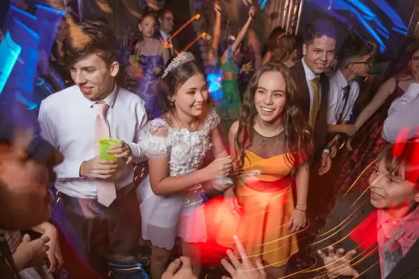 Des jeunes gens s'amusent lors d'une soirée bal, riant et dansant sous les lumières vives.