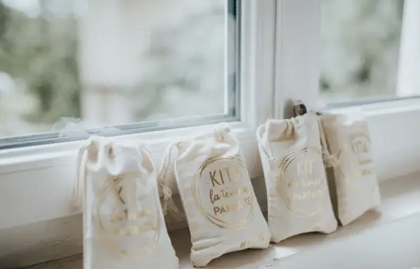 Quatre petits sacs en tissu écru, chacun portant l'inscription dorée "KIT du témoin PARFAIT". Un cadeau témoin mariage personnalisé, prêt à être offert.