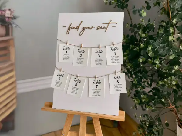 Un panneau "Trouvez votre siège" avec des cartes de table numérotées, chacune avec des noms d'invités. Un marque place vierge est visible sur la carte de la table 8.