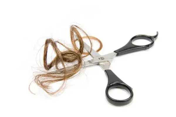 Ciseaux coupant une mèche de cheveux de bébé sur fond blanc.