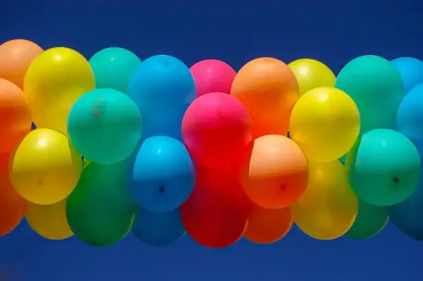 Un amas de ballons colorés flottant dans un ciel bleu. Combien de temps tient un ballon gonflé à l'air ? Cela dépend de sa taille et du matériau.