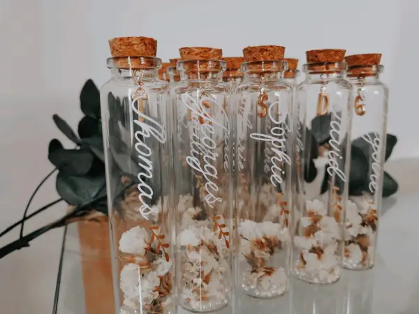 Bouteilles en verre avec fleurs séchées, bouchons en liège et breloques dorées. Parfait cadeau invité bapteme diy personnalisé avec des prénoms.