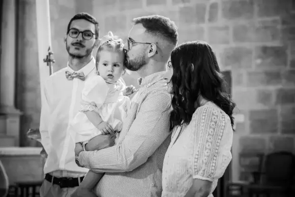 Un père embrasse sa fille, une petite fille en robe blanche, lors de son baptême. La question "jusqu'à quel âge peut-on baptiser ?" se pose.