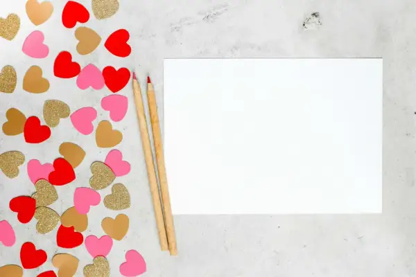 Cœurs rouges, roses et dorés pour une **journée Saint-Valentin** à écrire sur une feuille blanche avec deux crayons.