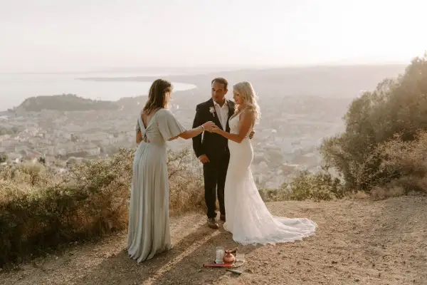 Cérémonie d'elopement mariage intime au sommet d'une colline, avec vue sur une ville et la mer. Le couple échange ses vœux, officiés par une amie.