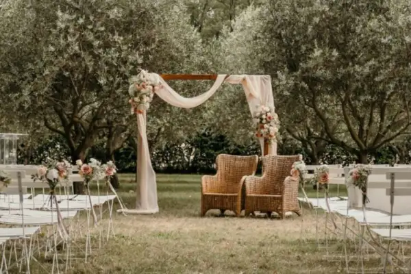 Un décor champêtre pour une célébration laïque : chaises blanches, arche fleurie, fauteuils en rotin sous les oliviers.