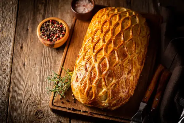 Un rôti en croûte dorée, prêt pour un menu de baptême à préparer la veille. Poivre et romarin à proximité.