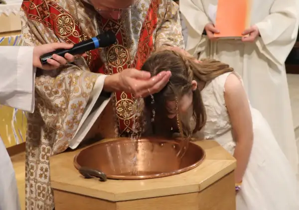 Cérémonie de baptême d'enfants : un prêtre verse de l'eau sur la tête d'une jeune fille dans une église.