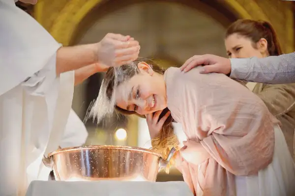 Une jeune fille souriante se fait baptiser à 16 ans. L'eau bénite coule sur sa tête, un moment émouvant.
