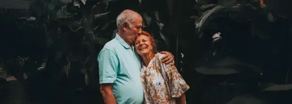 Un couple âgé s'embrasse tendrement, un moment de joie pour fêter sa retraite en famille.